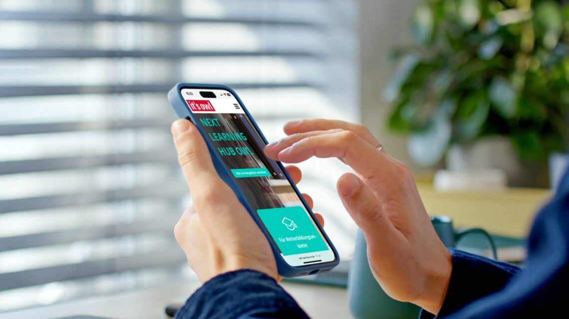 Person nutzt Smartphone mit geöffneter Website von it's OWL – Next Learning Hub OWL – zur Weiterbildung in OstWestfalenLippe. Moderne Lernplattform für digitale Qualifizierung und Weiterbildung in der Region OWL.